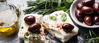 Feta cheese with olives and green herbs on gray marble background