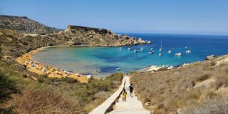 One of the beaches in Gozo, with people walking down stairs to a small bay