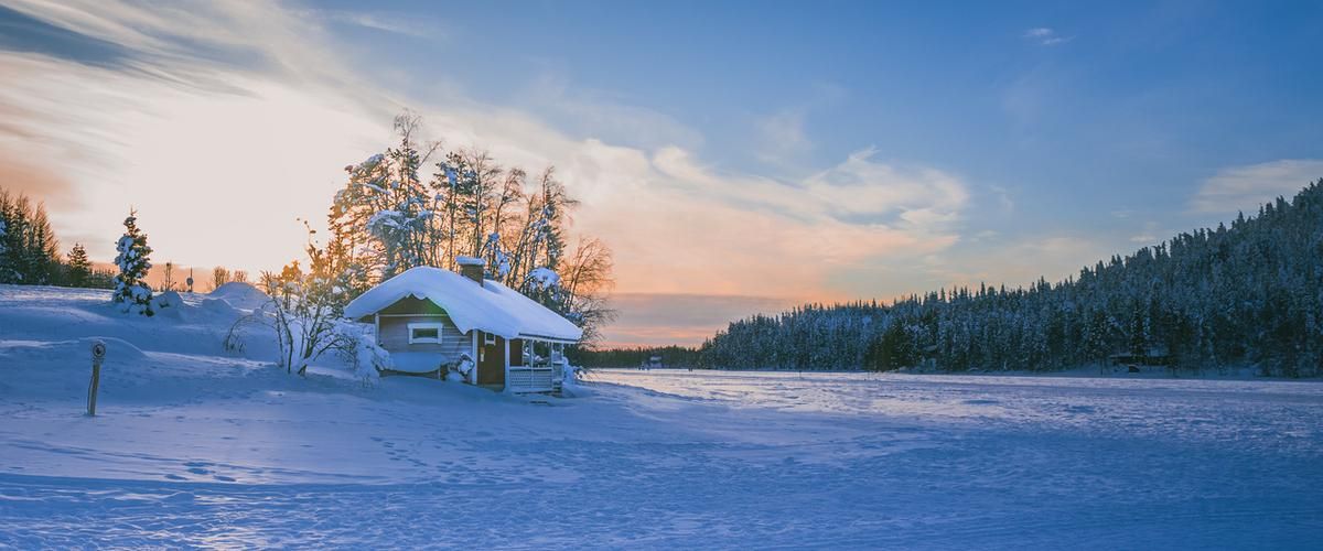 Cabin in a field full of snow at sunset