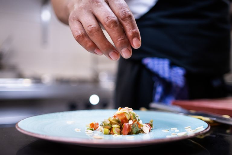 A hand finishing plating the food on the dish inside the restaurant kitchen