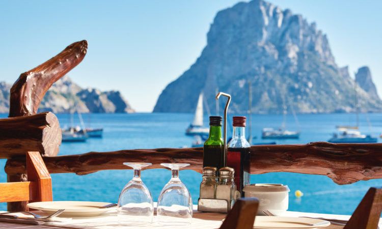 Outdoors restaurant at Cala d'Hort beach, with a fantastic view of the mysterious island of Es Vedra. Ibiza Island, Balearic Islands. Spain