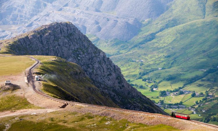 A train descends from the summit of Snowdon Mountain on the narrow gauge rack mountain railway with the Llanberis valley and spoil heaps of Dinorwig slate quarry in the distance. Wales