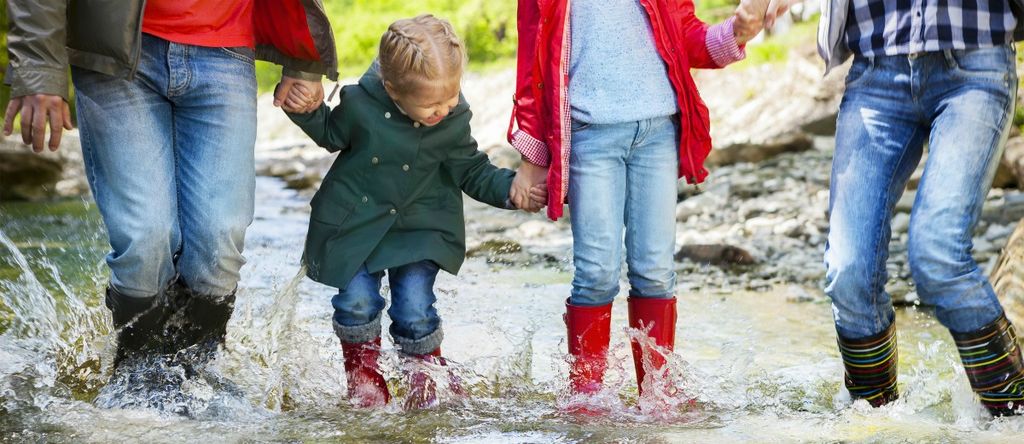 Happy family with two children wearing rain boots jumping into a mountain river