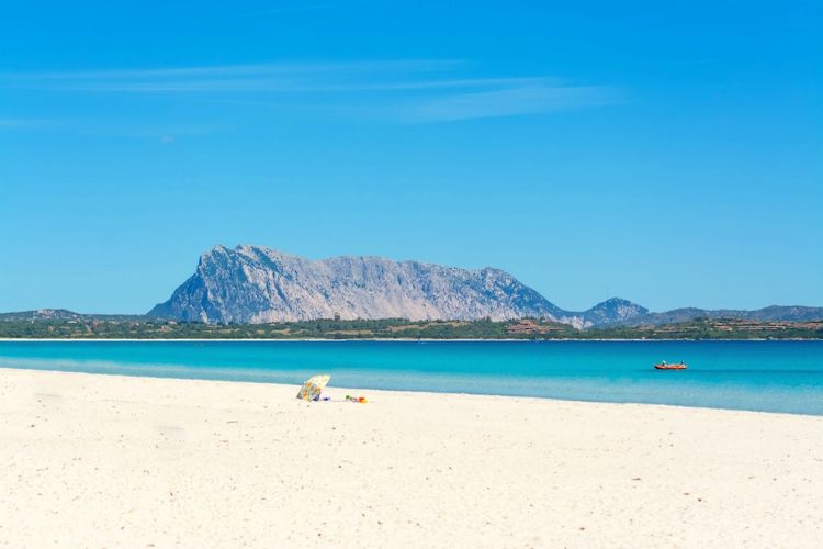 beaches in sardinia | white beach, blue water and mesa in the distance under blue skies | Spiaggia La Cinta
