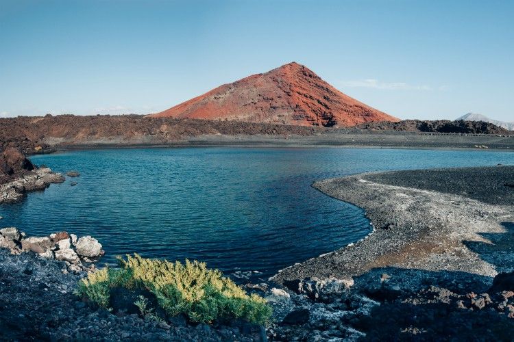 Panoramic view of unique volcanic landscape in Lanzarote island. Black sand, lake and and red mountain. Playa Bermeja. Travel destination. Nature background. unesco heritage. Canary Islands
