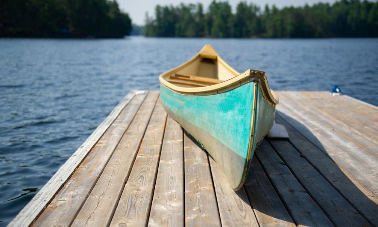 Green canoe rest on a lake wooden pier stock photo - slow travel